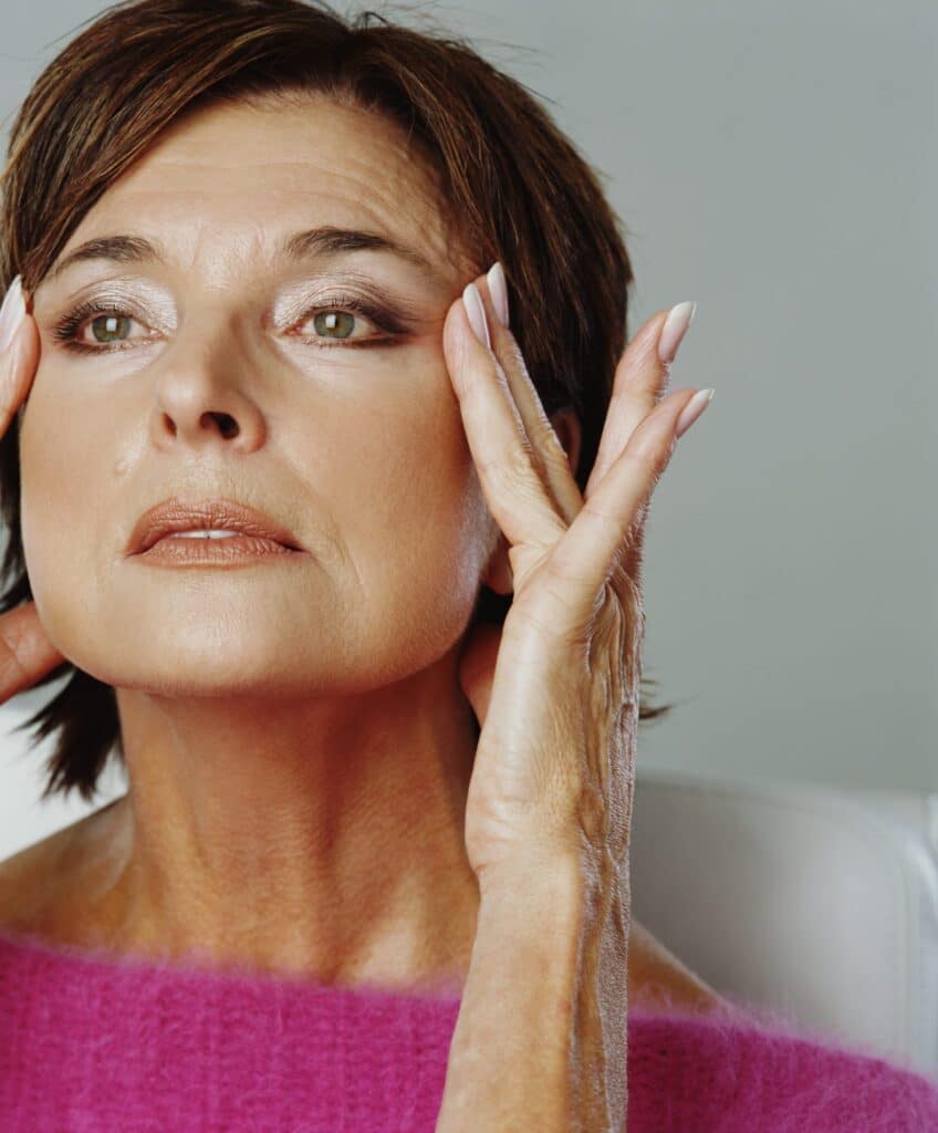 elderly woman looking herself at the mirror and touching her temples