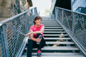 Woman sitting on city stairs in workout clothes holding a water bottle.