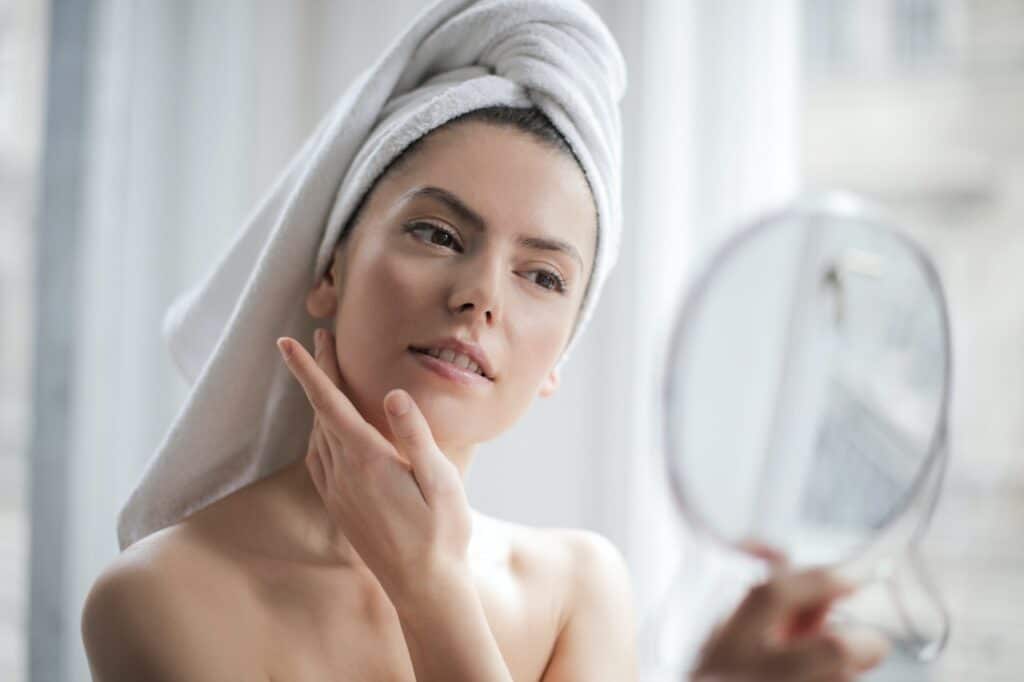 woman looking in mirror at face with hair in a towel