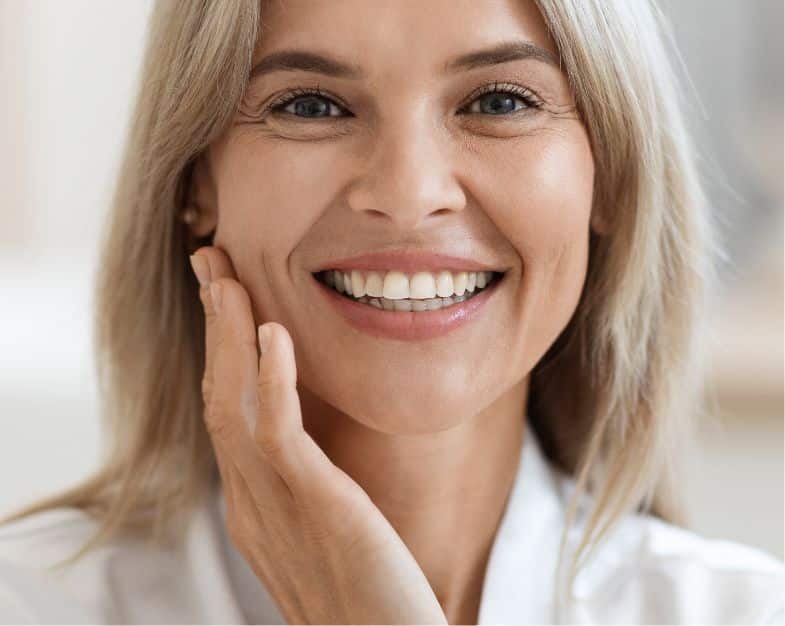 close up of older women smiling at the camera with her hand touching her chin