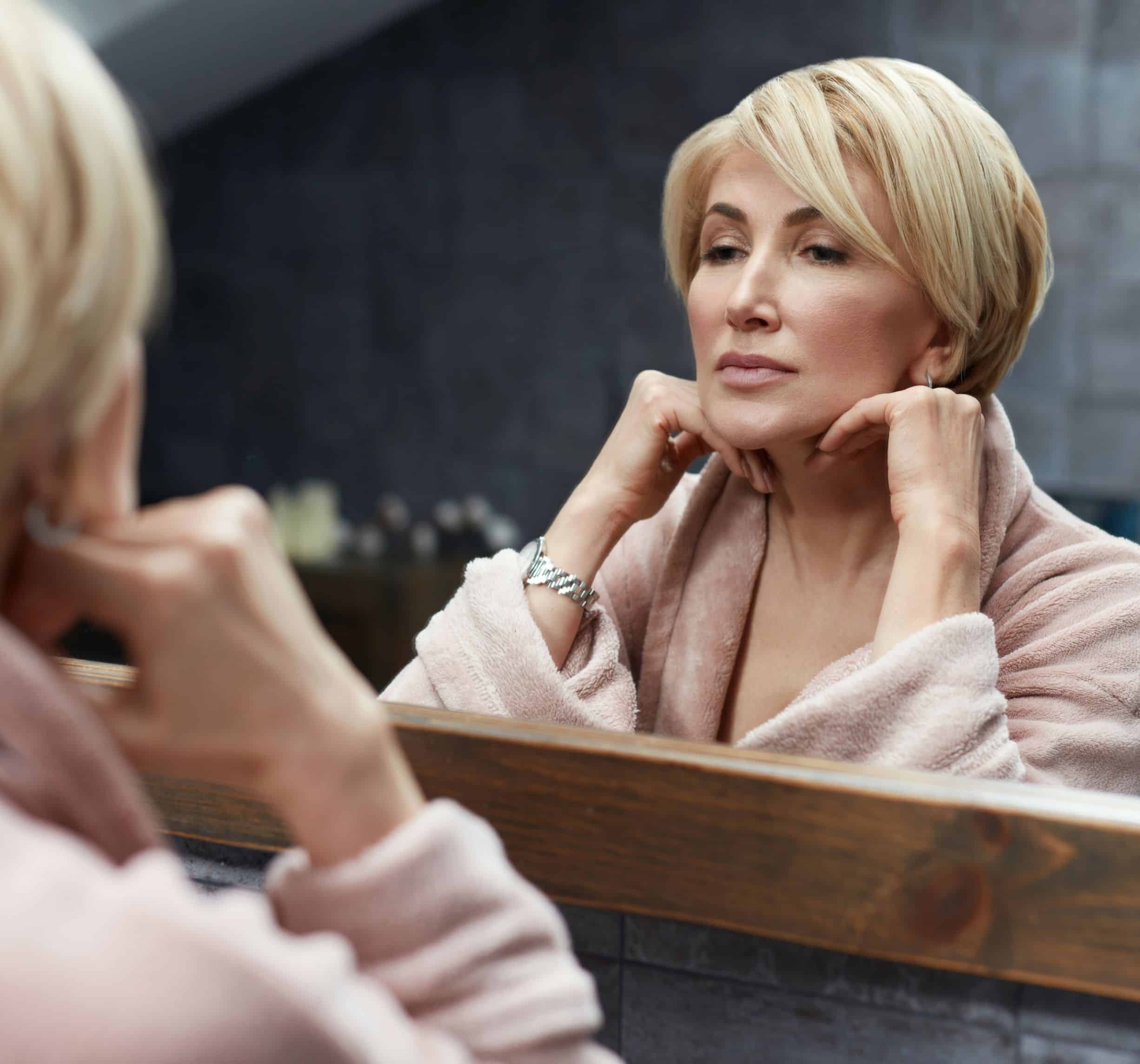 Middle-aged woman admiring her reflection after Fraxel laser treatment, showing smoother skin tone, reduced wrinkles, and rejuvenated complexion.
