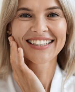 Smiling middle-aged woman touching her cheek, showcasing smooth, hydrated skin after SKINVIVE™ treatment.